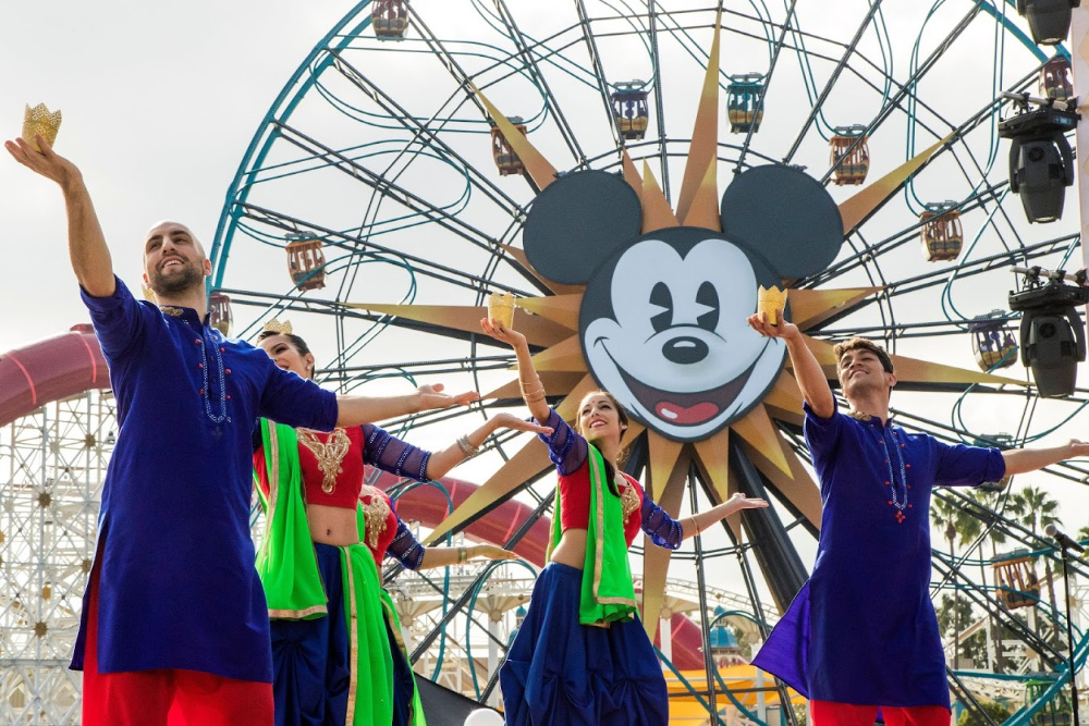 Grupo de bailarines de la India frente a la rueda de la fortuna de Mickey Mouse