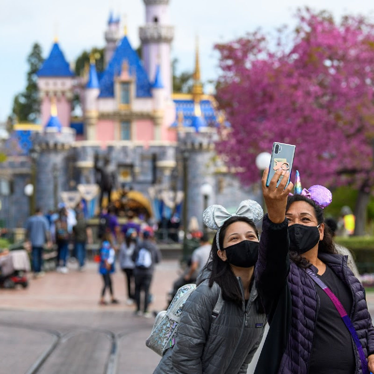 dos chicas con tapabocas tomándose foto enfrente del castillo durante la reapertura de Disneylandia